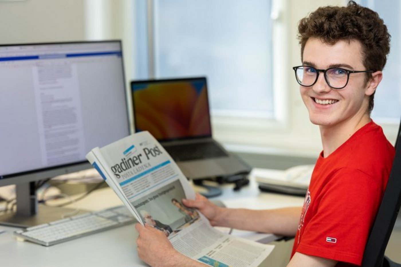 Portrait Fotograife eines Praktikanten in der Redaktion, welcher eine Zeitung in den Händen hält.