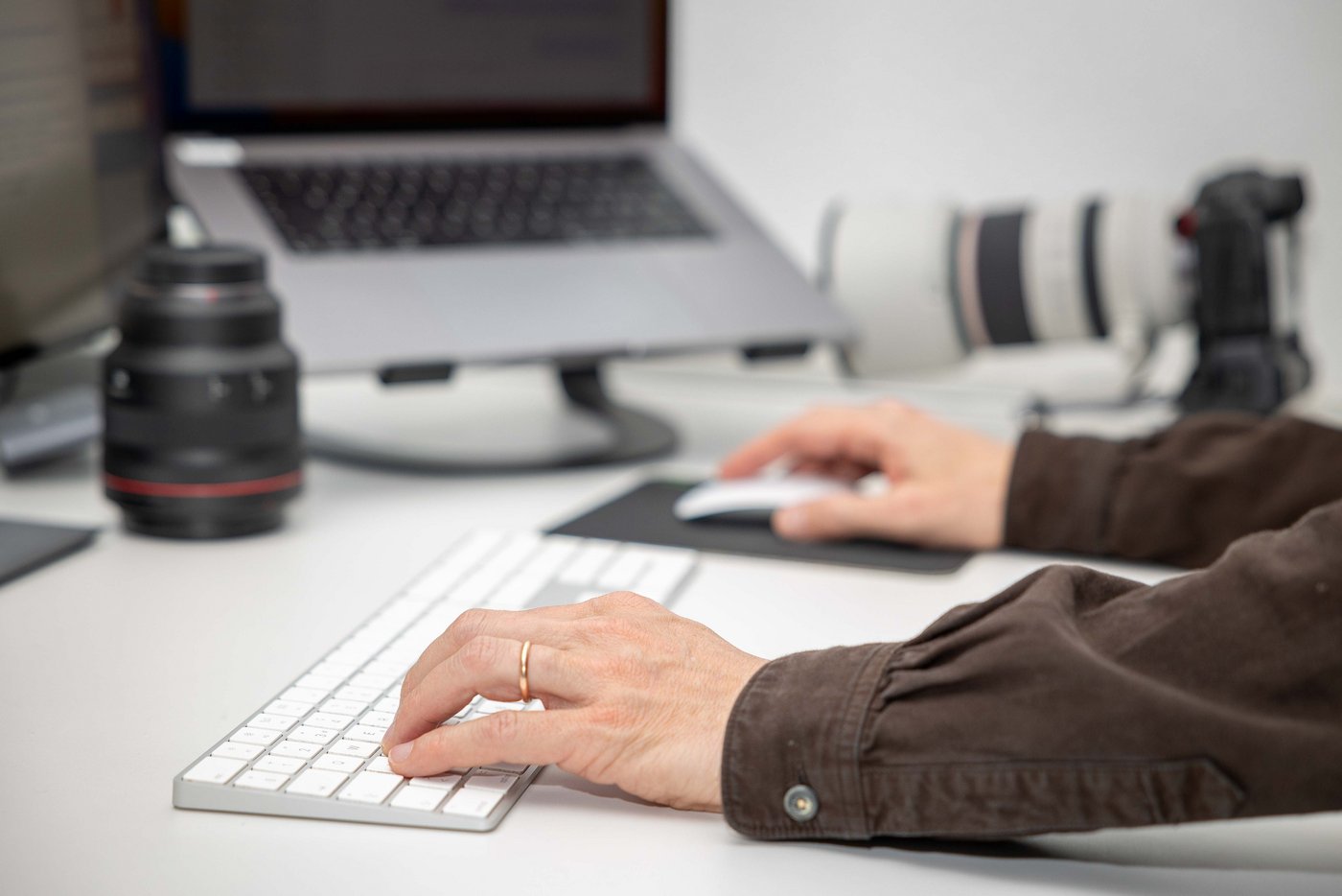 Nahaufnahme eines Redaktors, welcher am Bürotisch sitzt und text schreibt. Es sind verschiedene Objektive auf dem Tisch ersichtlich.